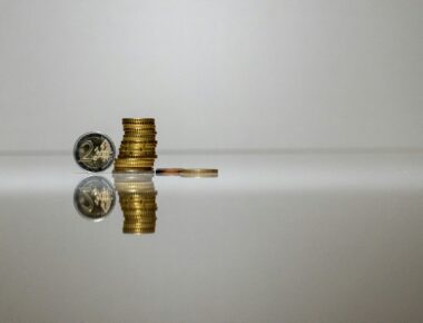 John Vid via Unsplash Een witte achtergrond en een spiegelende, witte ondergrond met daarom een stapeltje euro's die je in de spiegeling weer ziet.