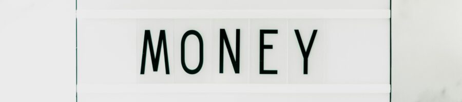 Image Hunter via Pexels Een witte marmeren achtergrond met op de voorgrond een wit bordje met 3 rijen. In de middelste rij is het woord Money te lezen in zwarte letters.