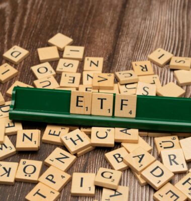 pexels-markus-winkler-1430818-18524062 Je ziet een houten tafel met daarop scrabble-letters. In het midden staat een scrabble-bordje met daarop de letters ETF. ETF's zijn in zichzelf producten waarmee je automatisch je beleggingen spreidt, omdat ETF's bestaan uit mandjes van aandelen.